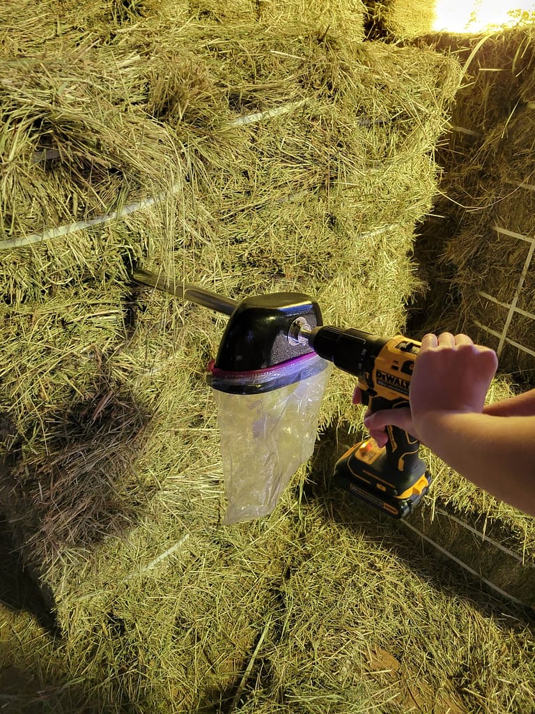 Close-up image of someone taking a hay sample using a bag attached to a drill